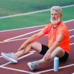Elderly man in athletic wear sitting on a track, resting after exercise.