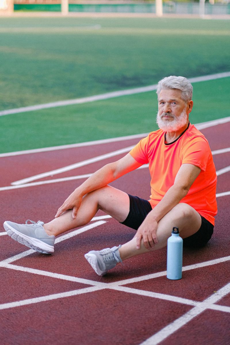 Elderly man in athletic wear sitting on a track, resting after exercise.