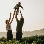 Side view of parents in casual clothes throwing excited son up while standing among lush green bushes in summer